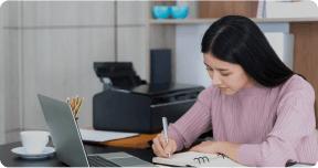 A student writing with laptop infront of them